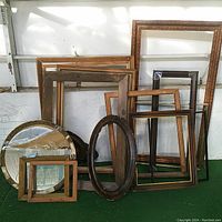 A group photo showing a variety of picture frames in different shapes, materials, and sizes arranged side by side on green carpet