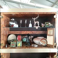 Photo of variety of vintage collectibles displayed on wooden shelves including glass jar, goblets, reindeer figurine, phone, pottery and memo pad holder.