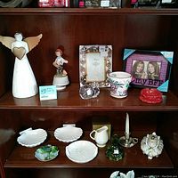 Wide shot of wooden shelf displaying all collectible items including wooden angel, porcelain figurines, shell plates, photo frames, and glass items