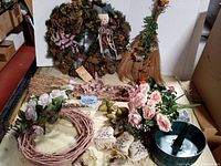 Photo showing a pinecone wreath decorated with a small plush snowman and ribbons, broom-style swag with dried flowers, a collection of twig wreaths, pink faux flower garlands, faux rose bouquets, fabric poinsettia flowers, and decorative holiday accents including painted egg ornaments and satin ribbons.