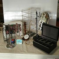 Various metal jewelry holders, acrylic drawer organizer, black jewelry box, wooden jewelry stand, and freestanding mirror arranged on a table.