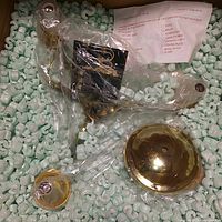 Chandelier components including brass ceiling plate and arms packed with green packing peanuts and assembly instructions.