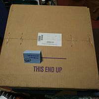 Closed cardboard box labeled 'White Brass Chandelier' with 'THIS END UP' marking and a small card indicating 'White Brass Chandelier'.