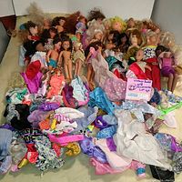 Full lot showing approximately 50 dolls and assorted clothing and accessories spread out on a surface.