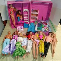 Full set of 10 dolls laid out in front of a pink Barbie carrying case with furniture and clothing items scattered around.