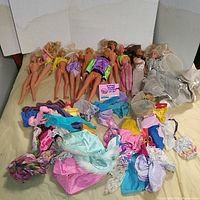 Lot of multiple vintage Barbie and Ken dolls laid out with a variety of colorful clothing pieces scattered around them, showing the extent and condition of the lot.