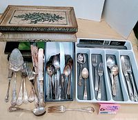 Photo showing all items in lot including wooden hinged box with floral design, Farberware flatware tray filled with silverware, and separate silverware pieces arranged in front