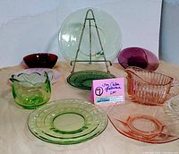 Photo of full lot showing 11 vintage colored Depression glass pieces including bowls, plates, and a creamer in green, red, pink, and purple colors.