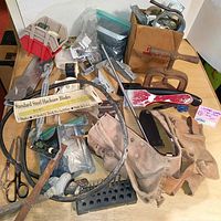 Overview of lot containing vintage leather tool belt, saw blades, painting tools, drill bits, clamps, and assorted hardware on table.