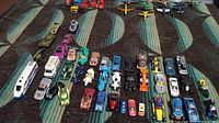 Overview of die-cast vehicles in multiple rows including cars, motorcycles, tanks, planes, and semi trucks on carpeted floor