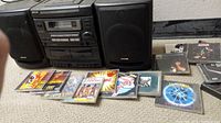 Full view of Aiwa boom box with two speakers and multiple classic rock CDs spread in front on carpeted floor.