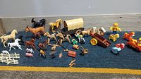 Lot of vintage farm animal toys including horses, pigs, fences, wagons, and toy figures with accessories arranged on carpet.