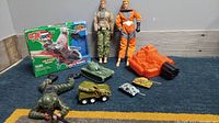 Full view of the toys including two GI Joe figures, boxed Cobra Raven, crawling army man, and various tanks and vehicles spread on the floor.