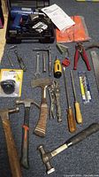 Full lot of hand tools laid on carpet showing hammers, wrenches, pliers, screwdrivers, pry bar, ranch suction cup and safety glasses.