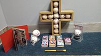 Wide view of lot showing homemade cross with used baseballs, collectible baseball in plastic case, mixed cards stacked in groups, and baseball pen.