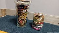 Photo of two large clear glass jars fully packed with assorted vintage jewelry items including beads, chains, rings, and bracelets.