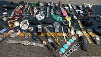 Wide view of a collection of various vintage and used watches and watch accessories arranged on a dark fabric surface.