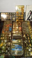 Overview of sectioned plastic organizers filled with assorted small jukebox electronic repair parts and components including diodes, capacitors, and potentiometers, plus a logic probe tester with leads.