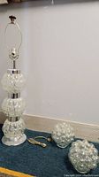 Full view of Mid-Century Modern chrome lamp with three bubble glass spheres stacked vertically and two separate bubble glass lamp shade bulbs on the floor nearby.
