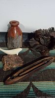 Photo showing the wood vase, wooden bird figurine on a base, abstract wooden sculpture, wood bark/root piece, and weaving device arranged on a patterned fabric background.