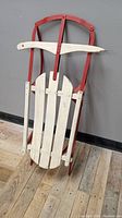Side angled view of the vintage Red Flyer snow sled showing red metal framing and white wooden slats.