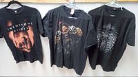 Three black rock band T-shirts hanging on hangers, shown side by side