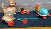 Four vintage toys grouped on floor: puppy squeeze toy, Corn Popper, wooden turtle and Whee-Lo dog pull toy.