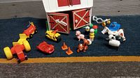 Photo showing red and white barn with multiple toy farm vehicles including tractors, toy farm animals including pig, cow, horse, dog, and toy farmer figures.