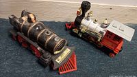 Side view of two train models on carpet, showing black porcelain decanter and the plastic toy train engine in silver and red colors.