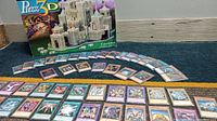 Photo showing Yu-Gi-Oh holographic cards fanned out in rows with Milton Bradley Camelot 3D puzzle box behind