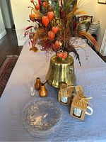 Wide angle photo of the whole lot including brass container, packaged mugs, wooden mills, glass shaker and glass plate on a table.