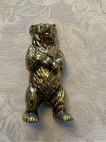 Top front view of brass bear bank on patterned fabric surface.