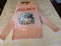 Front view of the pink knit Christmas sweater with sequined 'Boss Lady' face design and text.