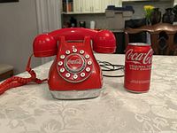 Front angle view of the red rotary Coca-Cola phone with a Coke can for size comparison.