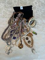 Photo showing various necklaces including faux pearls and beaded types, bangle bracelets in cream and metal colors, a pair of button-style earrings, and tribal design pendant necklace all arranged on a light fabric background.