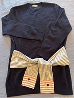Full front view of the black sweater laid flat with attached striped fabric belt tied in a bow.