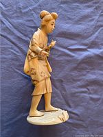 Full side view of carved ivory figurine showing the traditional kimono and base with damage.