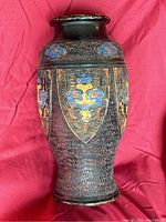 Front view of the ceramic vase showing the heraldry-like blue, red, yellow, and gold painted shields and motifs on a textured black surface.