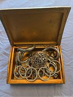 Open wooden jewelry box filled with silver-tone costume jewelry including chains, bangles, and a pendant.