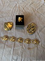 Four jewelry items on cream cloth: two brooches, ring on black holder, and bracelet with chain clasp spread out