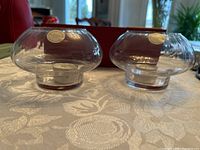 Pair of clear lead crystal tea light candle holders on table with patterned cloth background, each candle holder holding a tea light candle.
