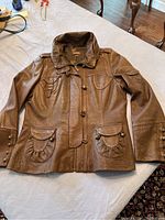 Full frontal photo of the brown leather jacket laid flat on a white surface, showing the entire jacket including collar, sleeves, and front pockets.