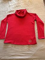 Full view of red long-sleeve cowl neck top laid flat showing ribbed texture and logo patch