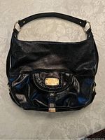 Front view of the black leather hobo style purse with gold plaque and strap on a light patterned surface