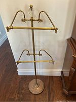 Full view of the entire brass towel rack including base, central pole, two towel bars and finial.