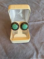 Front view of turquoise and marcasite earrings inside a cream jewelry box, showing details of stones and setting.