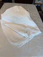 White twin cotton bedspread showing textured geometric pattern and knotted fringe edges, photo taken to display material and pattern detail.