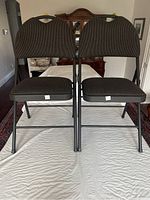 Front view of two black folding chairs on a table, showing padded striped fabric seats and backs.