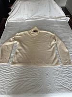 Full front view of the ladies white/light ivory cashmere sweater laid flat showing turtleneck collar and long sleeves.