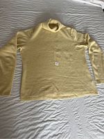 Full front view of a soft yellow cashmere sweater laid flat on a bed, showing the turtleneck and overall shape.